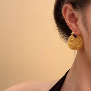 Close-up of elegant gold woven hollow ball earrings worn by a model in a warm setting