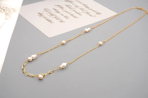 Detail of long gold necklace with freshwater pearls and oval links on a white card