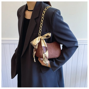 Détail du sac demi-lune en daim marron avec chaîne dorée et foulard en soie imprimé
