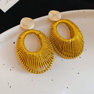 Détail de boucles d'oreilles ovales dorées avec texture tissée sur plateau blanc