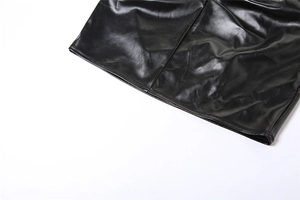 Macro shot of the black PU leather skirt hem showing asymmetric pleats and detailed texture