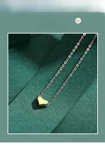 Close-up of polished gold heart pendant on a fine cross chain with elegant green backdrop