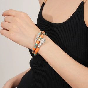 Close-up of a snake-shaped bracelet with orange and teal clay beads on a wrist