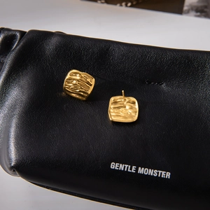 Detailed close-up of golden square earrings with hammered texture on black leather background