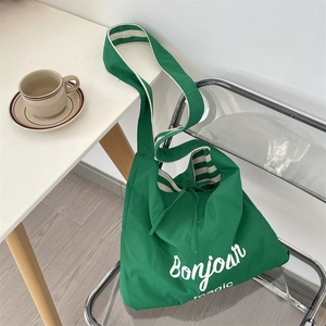 Detail of green canvas tote with Bonjour magic print and striped strap on a chair
