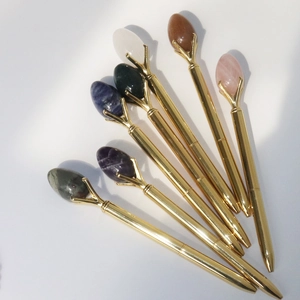 Detailed view of seven golden metal ballpoint pens with various colorful natural gemstones