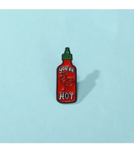 Macro detail of cartoon hot sauce bottle enamel pin with You're Hot text on blue background