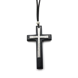 Detail of layered cross pendant featuring silver metal texture on black wood base