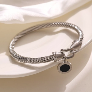 Macro detail of silver twisted cable bracelet featuring a black Roman numeral charm