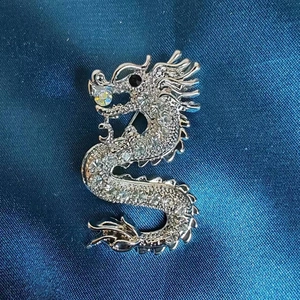 Detailaufnahme einer silbernen Drachenbrosche mit weißen Straßsteinen auf blauem Seidenstoff
