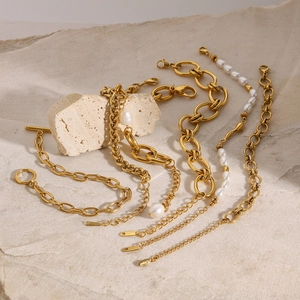 Set of five gold stainless steel bracelets with pearls and OT buckles on stone background