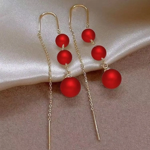 Detail of red bead tassel earrings in gold metal on a textured beige and silk background