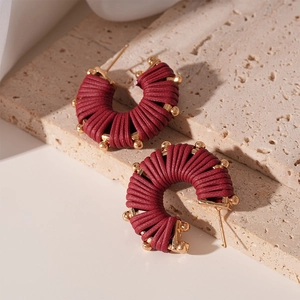 Macro detail of wine red woven thread C-hoop earrings with golden beads on stone stand