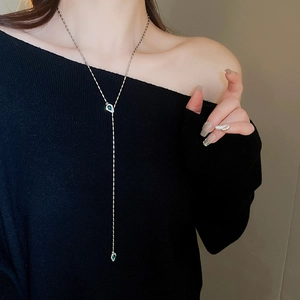 Detail of Y-shaped silver necklace with green pear-cut gemstones on black sweater