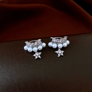 Macro view of silver star drop ear cuff with pearls and zircons on textured background