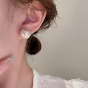 Close-up of a model wearing a single elegant white pearl stud earring with soft luster