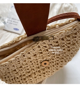Detail of a beige woven straw bag featuring a smooth metal zipper and magnetic buckle
