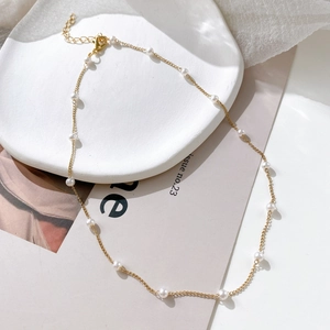 Close-up of elegant gold pearl choker necklace featuring round pearls on ceramic plate