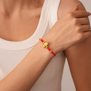 Detail of hand-woven red cord bracelet featuring a golden lucky mascot and beads