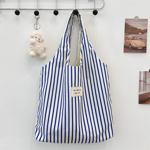 Détail d'un sac cabas en toile à rayures bleues et blanches avec écusson brodé et larges anses