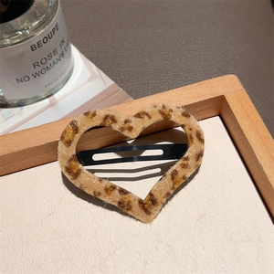 Close-up of a heart-shaped leopard print plush hair clip on a natural wooden tray