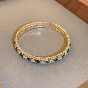 Macro detail of gold open bangle with emerald stones and white cubic zirconia pave setting