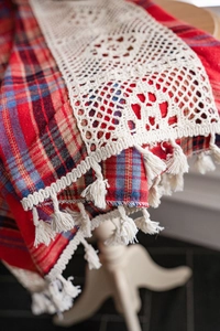 Detailed view of red and blue checkered fabric featuring beige lace trim and soft tassels