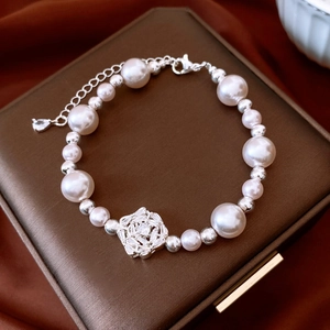 Close-up of elegant pearl bracelet with zircon flower pendant on dark silk background