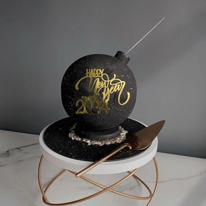 Detail of a black spherical New Year 2024 cake topper with gold text and a golden spatula