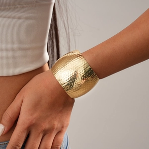 Close-up of a wide golden cuff bracelet featuring a unique hammered metallic texture