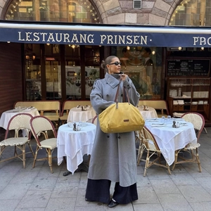 Elegante trench lungo grigio abbinato a una borsa da viaggio gialla in tela e pelle