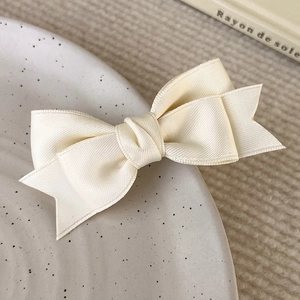 Close-up of cream satin bow hair clip with dual-layer texture on a ceramic dish