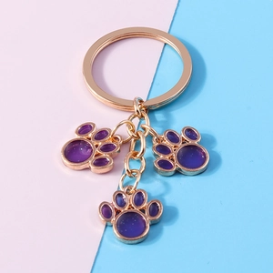 Golden keychain featuring three purple cat paw resin pendants on pink and blue background