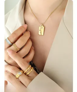 Nahaufnahme von goldenem Anhänger mit Gesichtsgravur und schlichten Ringen an der Hand
