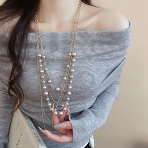 Detail of layered artificial pearl necklace on a model wearing a grey sweater