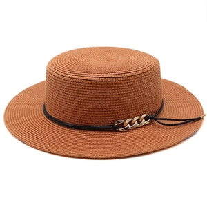 Détail d'un chapeau canotier en paille marron avec cordon noir et chaîne dorée sur fond blanc