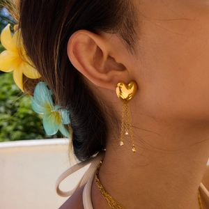 Golden stainless steel heart tassel earrings with crystal drops worn by a model