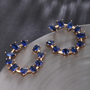Detail of C-shaped gold earrings featuring mixed-cut navy blue zircon gemstones
