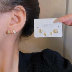 Three-pair set of gold and enamel geometric earrings shown on model and packaging