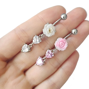 Vue détaillée de piercings de nombril avec roses et cristaux en forme de cœur sur la main