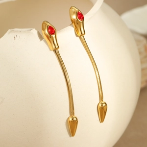 Detail of gold snake earrings with red gems and thin chain on a white ceramic vase