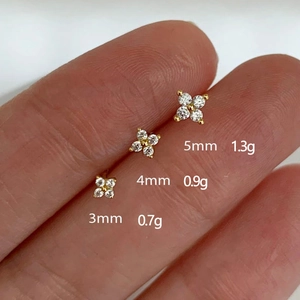 Three sizes of gold flower stud earrings with zircons shown on finger for scale