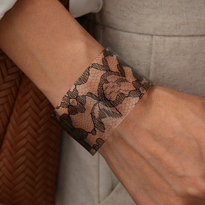Macro shot of wide open acrylic bangle with intricate black lace patterns on an arm