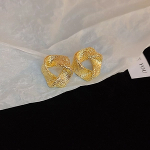 Macro shot of gold geometric earrings with hammered metal texture on white creased paper