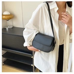 Minimalist black leather saddle bag with gold hardware worn over a white shirt
