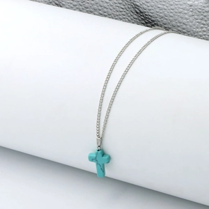 Close-up of a turquoise stone cross pendant on a fine silver chain over white surface