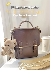 Detail of cute plush elephant keychain in khaki hanging on a vintage leather bag