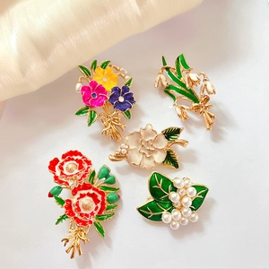 Close-up of enamel flower brooches with pearl accents on white silk background