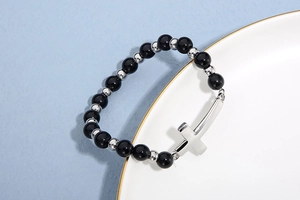 Gros plan d'un bracelet en perles noires avec croix argentée sur une assiette blanche