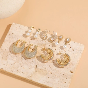 Detailed close-up of gold-plated earrings with pearls and cubic zirconia on a stone tile